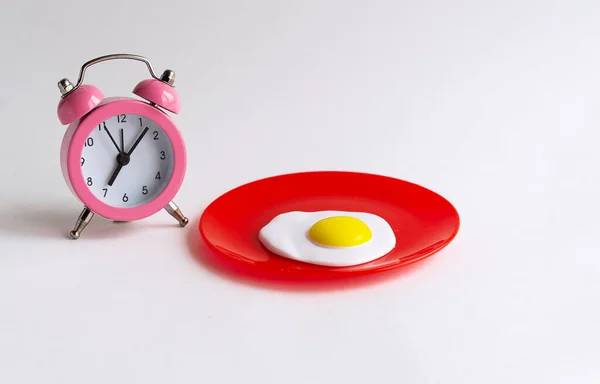 Kahvaltı vakti geldi. Klasik pembe çalar saat sabah 7 'yi gösteriyor. Kırmızı tabakta sahanda yumurta. 