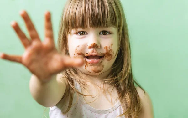 可愛くて甘い女の子で チョコレートを顔と指に塗りました 汚れた顔をした幸せな少女が笑っている 幸せな子供時代の概念 7月7日のチョコレートのお祝い ストック写真
