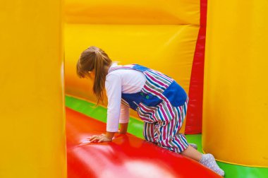 Aktif bir küçük kız renkli şişme bir slaytta oynuyor. Küçük bir çocuk şişme trambolinde eğleniyor. Mutlu, eğlenceli bir çocukluk. Çocuklar için eğlence. Çocuklar için aktif oyunlar