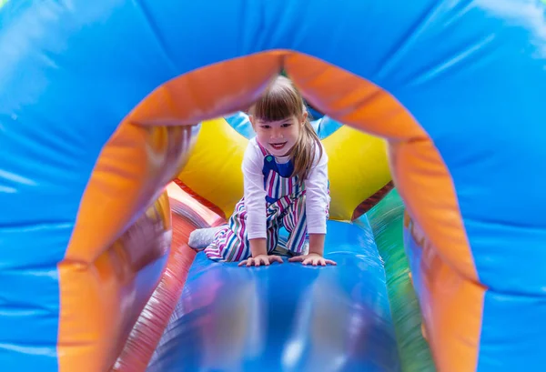 A little girl plays in an inflatable attraction at an amusement park on weekends. Cute baby on an inflatable trampoline. An Active Child Having Fun In A Sports Center. Cute happy baby. Game Time