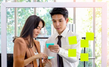 Asyalı iş adamları ve kadınlar beyin fırtınası için post-it arıyor ve yazıyor. Ofisteki çalışma planına, beyin fırtınasına, stratejik yaratıcı yaşam tarzına, İş Konseptinde Başarı 'na aynaya bir yazı yaz.