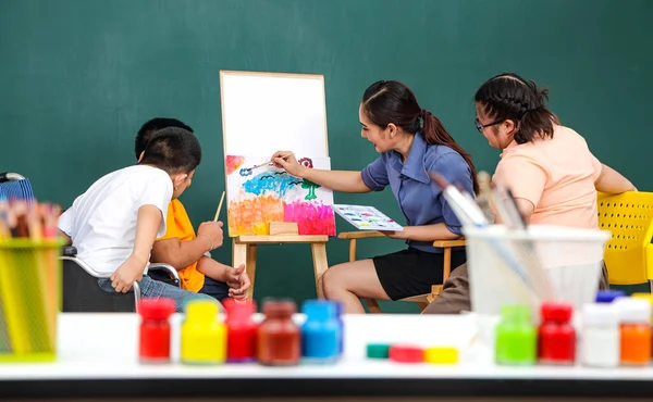 A group of young girls with disabilities and autism is training their hand and finger muscles by drawing and painting with water. With the help of teachers Happy and focused in the classroom