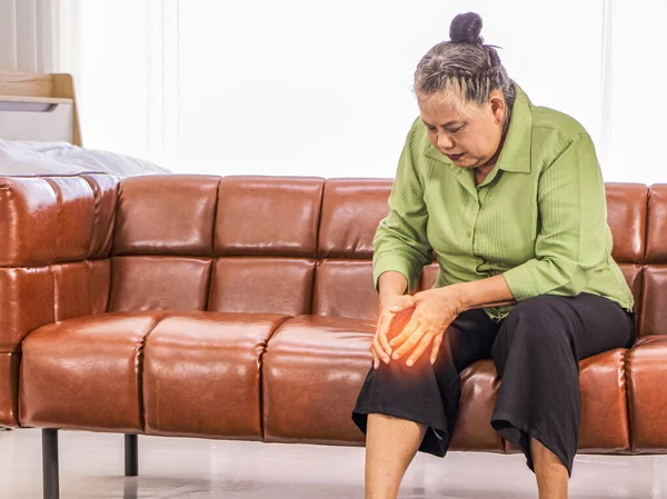 アジアの高齢女性部屋のソファに座っている間 痛みで膝を保持健康管理の概念膝の痛み 健康上の問題に苦しんでいる女性シニア女性と人々の概念 — ストック写真