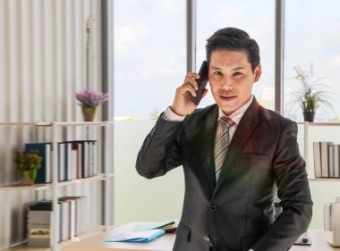 Siyah takım elbiseli genç bir işadamı akıllı telefonunu kullanarak iş dünyasının konseptini parlatmaya ve uzay boşluğunu kopyalamaya çalışırken mutlu bir şekilde gülümsüyordu.