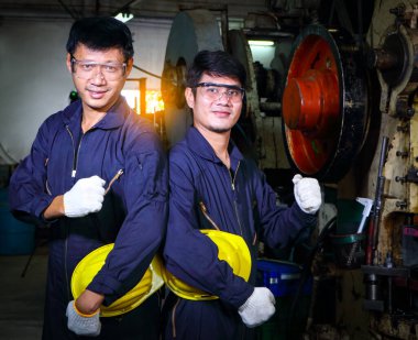 Miğfer üniforması giymiş iki yetenekli Asyalı işçi teftiş verilerini analiz etmek için konuşuyorlardı. Metal baskı makinesinin bakımı Fabrikadaki takım çalışması kavramı