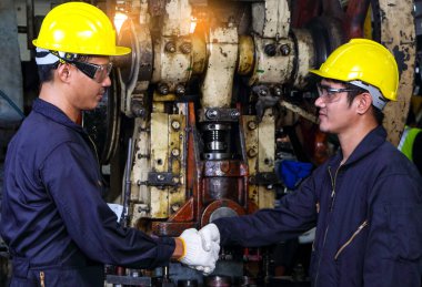 Üniformalı iki yetenekli Asyalı işçi elleriyle konuşuyor ve birbirlerine dokunuyorlardı. Metal pres makinesinin bakımı tamamlandığında, fabrikadaki takım çalışması kavramı.