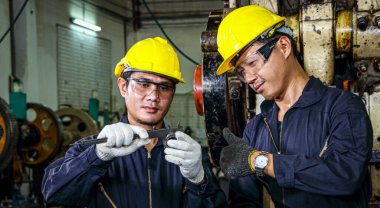 Güvenlik giysileri içinde iki Asyalı erkek işçi Vernier Calipers kullanıyor. Çalışan makinelerin endüstriyel fabrikalar ve üretim süreçlerindeki yedek parçalarını inceleyin ve ölçün.