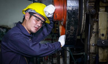 Üniformalı, kasklı ve güvenlik gözlüklü Asyalı bir erkek işçi işten sonra şekerleme yapıyor, teftiş yapıyor, fabrikada metal presi tamir ediyor..
