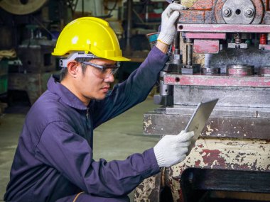 Üniforma, güvenlik şapkası ve güvenlik gözlüğü takan yetenekli Asyalı işçiler. Verileri analiz etmek için bir tablet kullanılıyor Metal basın bakım denetimi fabrikada, takım çalışması konsepti