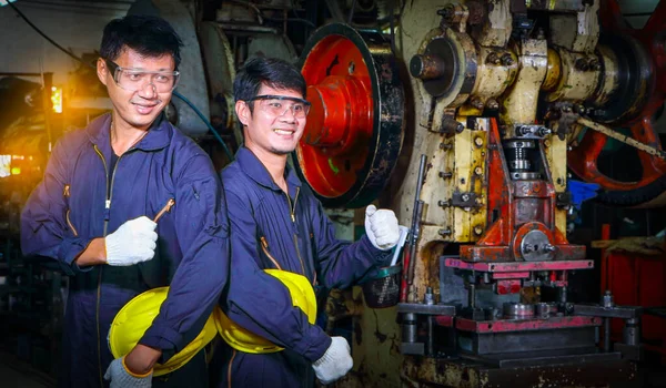 Miğfer üniforması giymiş iki yetenekli Asyalı işçi teftiş verilerini analiz etmek için konuşuyorlardı. Metal baskı makinesinin bakımı Fabrikadaki takım çalışması kavramı