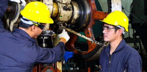 Miğfer üniforması giymiş iki yetenekli Asyalı işçi teftiş verilerini analiz etmek için konuşuyorlardı. Metal baskı makinesinin bakımı Fabrikadaki takım çalışması kavramı