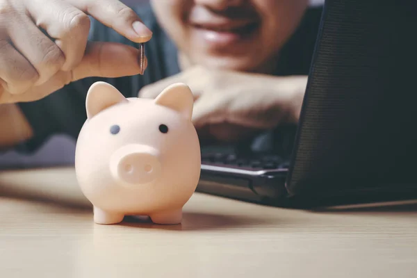 Cute pig piggy bank on the wood floor. Working with Asian men who are enjoying saving frugal coins at home during a crisis, reduce family expenses. Concept of saving money for future family expenses