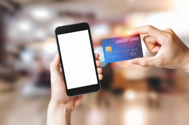 Akıllı cep telefonlu eller alışveriş merkezinin arka planında, elektronik ödeme teknolojisinde, internet bankacılığı kavramında online alışveriş için beyaz arka plan gösteriyor.