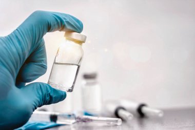 Doktorun elinde önleme, bağışıklık ve kovid 19 enfeksiyonu ya da koronavirüs tedavisi için aşı ve şırınga var. Hastalık önleme kavramları. Aşı şişesine odaklan, geçmişi bulanık..