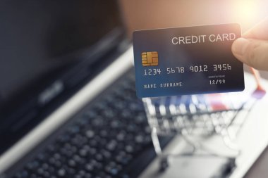 Kredi kartı tutan eller ve evde fotokopi alanı olan online alışveriş için dizüstü bilgisayar kullananlar. E-ödeme teknolojisi, alışveriş kolik yaşam tarzı, internet bankacılığı kavramı, kredi kartı modeli