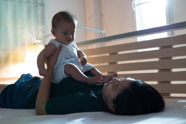 Genç Asyalı anne yatağa uzanıp yatmadan önce yatak odasında rahatlamak için kızıyla oynuyor..