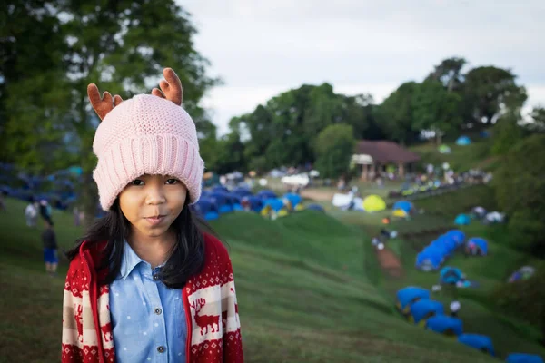 亚洲小女孩头戴一顶暖和的帽子 站在青草山岗上与家人露营 享受美丽的大自然的画像 — 图库照片