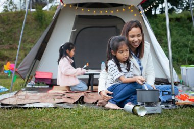 Şirin Asyalı kız, ailesiyle kamp yaparken annesine çadırın dışında yemek yaparken yardım etmek için eğleniyor..