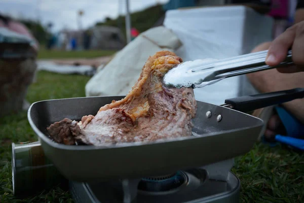 Close up on woman grilled pork barbecue in the picnic pan and cooking food for friend and family while camping with family in the camping site.