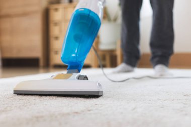 Kadın oturma odasındaki halıyı temizlerken elektrikli süpürgeyi kapat. Asyalı kadın evde ev işi yapıyor..