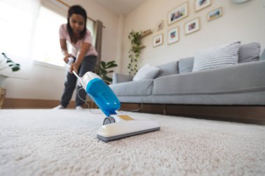 Kadın oturma odasındaki halıyı temizlerken elektrikli süpürgeyi kapat. Asyalı kadın evde ev işi yapıyor..