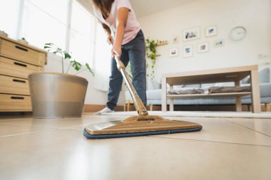 Asyalı bir kadın oturma odasında mikrofiber ıslak bezle yerleri temizleyip paspaslıyor. Evde ev işi yapan bir kadın. Oda servisi kavramı.