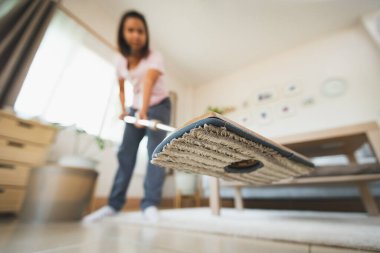 Asyalı bir kadın oturma odasında mikrofiber ıslak bezle yerleri temizleyip paspaslıyor. Evde ev işi yapan bir kadın. Oda servisi kavramı.