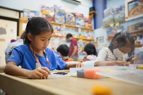 Asian child girl and sister wearing protection mask making fusible beads thermo mosaic in pegboard that is a toy to develops the imagination of child during Coronavirus pandemic.