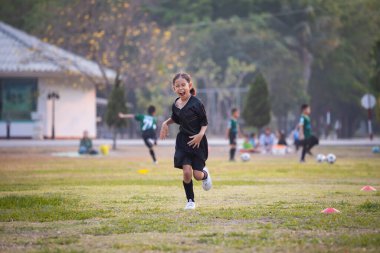 Asyalı kız komik surat yapıyor ve futbol sahasında mutlulukla koşuyor. Çocuk oyunda kazandıktan sonra mutlu olur. Çocuk spor eğlencesi konsepti.