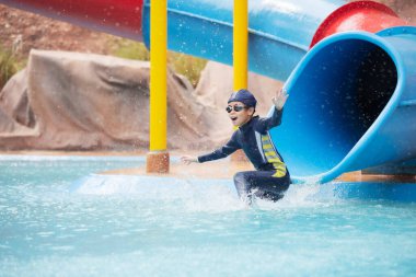Asyalı bir çocuk yazın su parkında su kaydırağında kayarken eğleniyor..