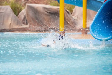 Asyalı bir çocuk yazın su parkında su kaydırağında kayarken eğleniyor..