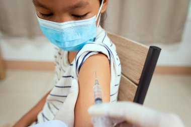 Doktor, Asyalı çocuk koluna aşı yapıyor. Coronavirus Covid-19 salgınını korumak için maske takan çocuk. Sağlık ve tıbbi konsept.
