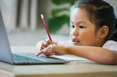 Asyalı kız öğrenci, internetten öğretmeniyle video görüşmesi yapıyor. Covid 19 salgını nedeniyle karantina sırasında bilgisayarda evde eğitim görüyor..