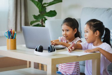 İki Asyalı çocuk öğrenci, öğretmenleriyle birlikte internetten video görüşmesi yapıyor. Kardeşler Covid 19 salgınından dolayı karantina sırasında bilgisayarla evde eğitim görüyorlar..