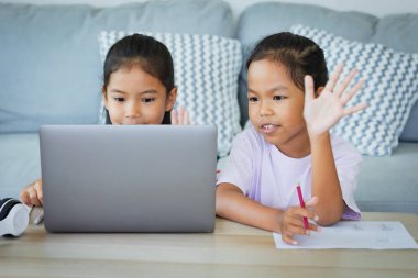 İki Asyalı çocuk öğrenci, öğretmenleriyle birlikte internetten video görüşmesi yapıyor. Kardeşler Covid 19 salgınından dolayı karantina sırasında bilgisayarla evde eğitim görüyorlar..