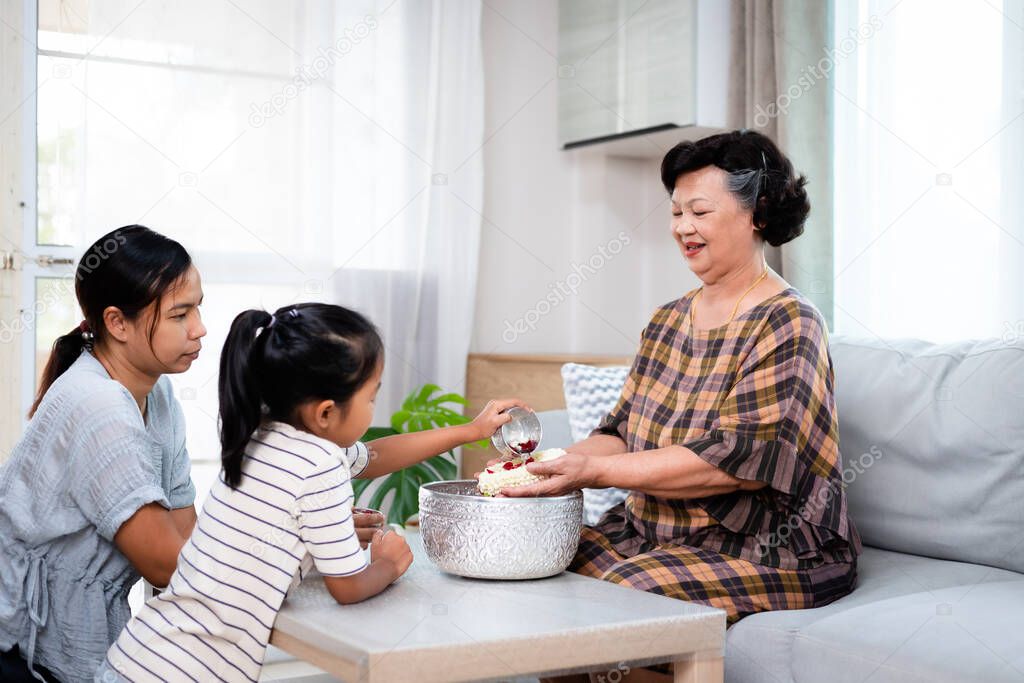Asian child girl and her mother pouring water on hands of elder senior or respected grandparents for celebrate Songkran in new year water festival.