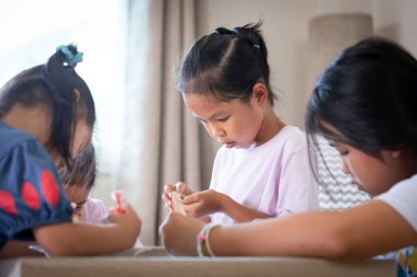 Asyalı kız ve arkadaşları parti için kurabiyeleri eğlenceli bir şekilde süslüyorlar. DIY ev yapımı çocuk sanatı ve zanaat konsepti.