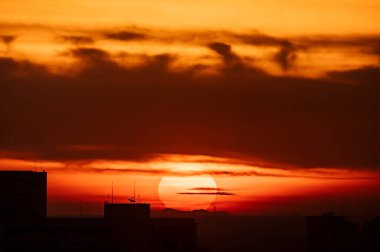 Arka planda bulutlu gökyüzü olan büyük yuvarlak turuncu gün doğumu, süper telefoto lensli görüntü