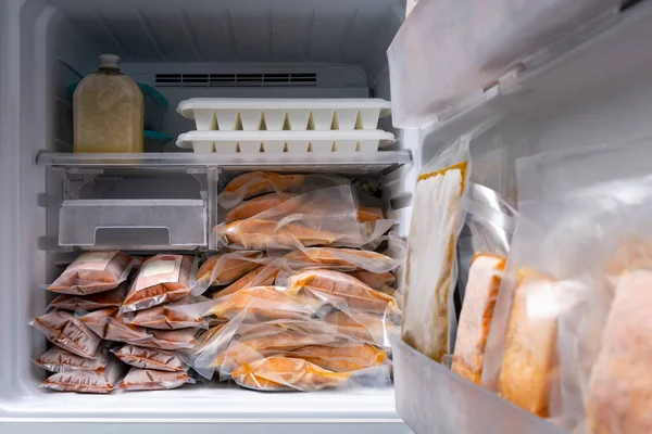 freezer of modern frigerator full with frozen food products in quarantine or work from home period during coronavirus pandemic, freeze cooked salmon in vacuum packs