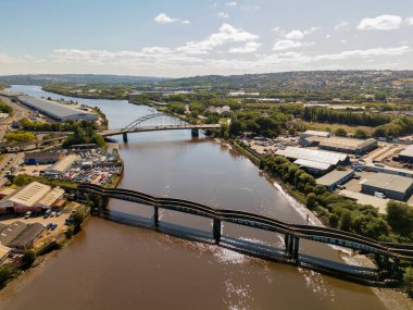 Tyne UK 'deki Newcastle: 15 Ağustos 2025: Scotswood Demiryolu Köprüsü Tyne Nehri' ni geçer. Manzarada nehir kıyısı boyunca sanayi binaları, araçlar ve yeşil alanlar yer alıyor.