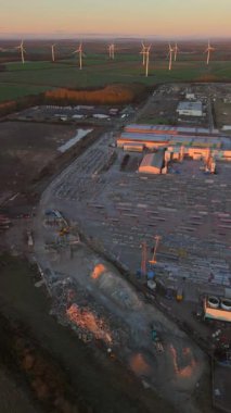 Lynemouth UK: 31 Aralık 2025: Yapım öncesi üretim ürünleri, makineler, binalar ve kamyonlar üreten bir üretim tesisi. Rüzgar türbinleri şafakta arka planda görünür.