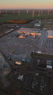 Lynemouth UK: 31 Aralık 2025: Yapım öncesi üretim ürünleri, makineler, binalar ve kamyonlar üreten bir üretim tesisi. Rüzgar türbinleri şafakta arka planda görünür.