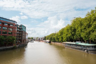 Bristol UK: 28 Temmuz 2025: Bristol besleme kanalı, tekneler suda yüzüyor. Binalar dağılmış bulutlarla temiz bir gökyüzünün altında sıralanır.