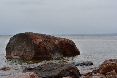 Kıyıya yakın pembe bir granit kaya bulutlu bir Baltık gününde Narva Körfezi 'nin sakin sularından dışarı çıkar. Çiseleyen yağmurdan dolayı ufuk pusludur..