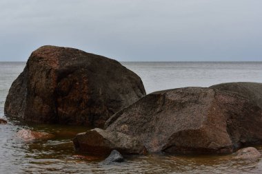 Narva Körfezi 'nin sakin sularında, bulutlu Baltık gökyüzünün altında, zamanla kararmış iki pembe granit kayanın yakın çekimi..