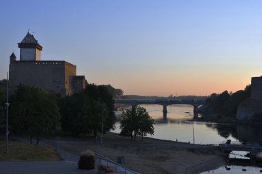 Narva Kalesi ve Narva sınır nehri şafakta bir köprüye sahip, güneş henüz görünmüyor, ama ışınları çoktan gökyüzünü ve şatoyu sarıya boyamaya başladı..