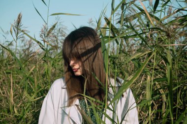 Genç bir kadın yeşil bir boğa içinde gözleri kapalı, seçici bir odak noktası ile dışarıda bekliyor.