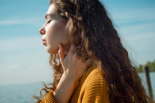 Primer plano de la hermosa mujer joven con el pelo rizado usando en suéter amarillo en una playa — Foto de Stock