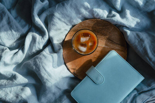 Вид сверху на стекло с ледяным кофе и планировщик на деревянной дорожке на синем льняном одеяле