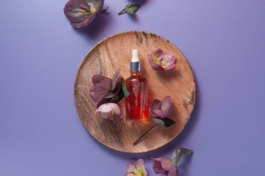 Ahşap bir tabakta doğal organik C vitamini serumu. Etrafı pastel menekşeli çiçeklerle çevrili.,